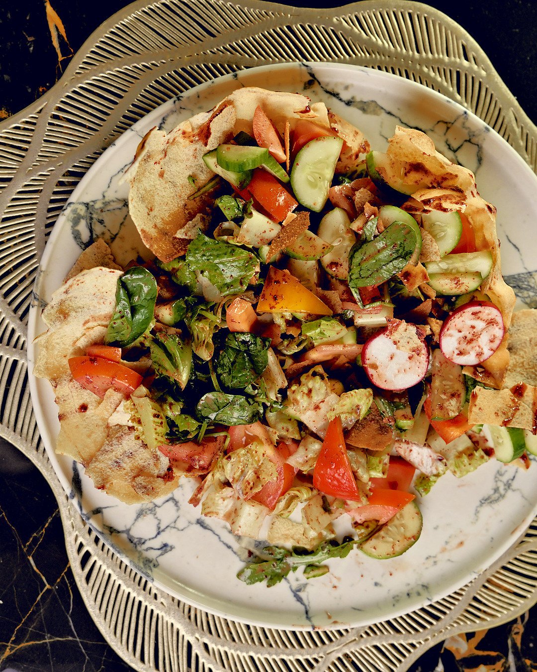 Fattoush with crisp bread, radish and tomato on a marble-veined plate