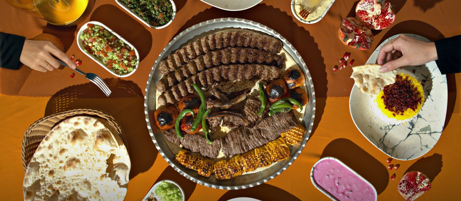 The whole Joon table from above: bread, small plates, the Mixed Kebab Platter, saffron rice and pomegranates on a burnt-orange cloth
